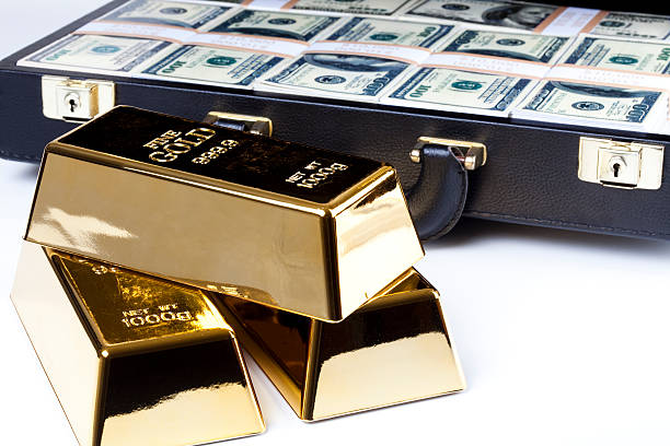 Lingotti d’oro lucenti davanti a una valigetta piena di banconote in dollari, simbolo di valore e investimento.